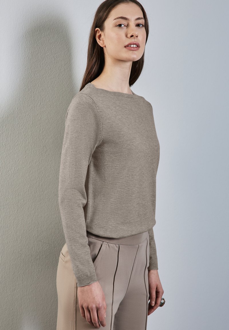 Lichtbruine gebreide trui met lange mouwen en een ronde halslijn, gecombineerd met hooggetailleerde beige broek met voorklauwen.