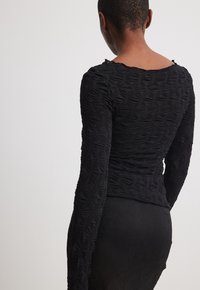 Haut noir à manches longues en tissu texturé avec un motif d'étoiles en relief, col arrondi et coupe ajustée.