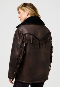 Rudos spalvos odinė striukė su juodos dirbtinės kailio apykakle, su kutais šonuose ir nugaroje. Lygus paviršius, laisvo silueto.