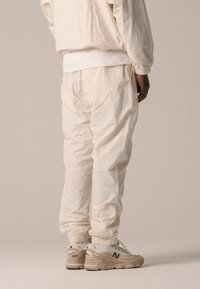 Une tenue de sport légère de couleur crème avec un motif texturé. Pantalons fuselés avec des poignets élastiques, associés à des baskets beige avec un logo.