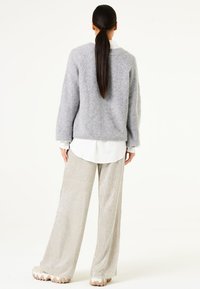Grauer Strickpullover mit geripptem Muster, darunter ein weißes Hemd mit Kragen, kombiniert mit glänzenden silbernen Weitbein-Hosen und klobigen beigen Schuhen.