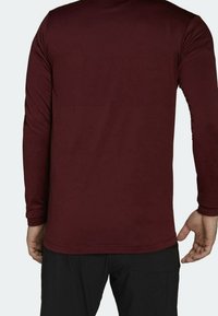 Camisa de manga larga color marrón oscuro, hecha de tela texturizada, con un escote redondo y un dobladillo liso, mostrada desde atrás.