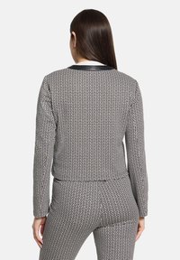 Ensemble veste cintrée et pantalon à motif quadrillé noir et blanc, avec manches longues et col contrastant. Tissu lisse, coupe ajustée.