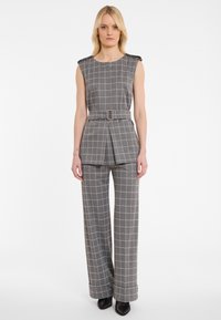Grijs geruit pak met wijd uitlopende broek en een riem in de taille. Bevat een mouwloze top met schouderaccenten en een gladde textuur.
