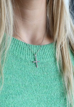 Collier avec pendentif croix en argent sterling sur une fine chaîne, présentant une surface texturée, porté sur un pull en vert à côtes.