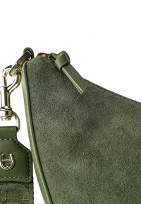 Bolso de ante verde con una correa de cuero suave, que cuenta con un clip de herrajes en tono dorado. La forma es curva, con detalles de costuras visibles.