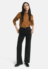 Brown corduroy button-up shirt, black high-waisted wide-leg pants, smooth texture, with black loafers. Simple, classic clothing ensemble.