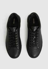 Zapatillas de piel negra con un acabado suave, presentando una puntera redonda, un diseño de cordones con seis ojales y una suela de goma de perfil bajo.