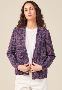 Blazer blu navy con un motivo floreale in rosso e bianco. Presenta un colletto a punta e apertura frontale, abbinato a una t-shirt bianca sottostante.