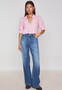 Chemise à rayures rose pâle avec des manches retroussées, associée à un jean en denim bleu taille haute et à jambes larges. Des chaussures noires complètent le look.