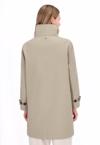 Bézs vízálló kabát magas gallérral, hosszú ujjal, gombos mandzsetta díszítéssel, és elegáns, letisztult, minimalista dizájnnal.