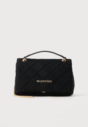 Sac à main Valentino noir matelassé avec une bandoulière chaîne dorée, un logo doré et une poignée supérieure, posé sur un fond clair uni.