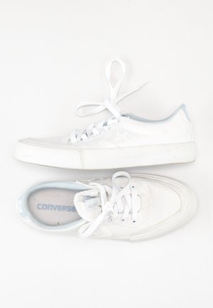 Bílé plátěné tenisky se světle modrými detaily, kulatou špičkou, gumovou podrážkou a klasickým zavazováním na tkaničky. Uvnitř je viditelné logo značky.