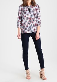 Blomstermønster skjorte i hvid, rød og blå, med trekvartærmer og nøglehulknap. Kombineret med mørke skinny jeans og nude blockhæle.