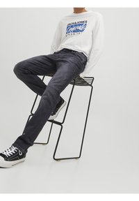 Mörkgrå jeans i denim med rak bendesign. Kombineras med en långärmad vit t-shirt med grafik och svarta sneakers.