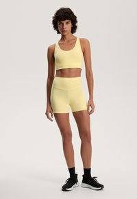 Rumena atletska modra in visoko pasne kratke hlače, narejene iz raztegljivega blaga, z gladko teksturo in preprostim dizajnom. Vključene so tudi črne atletske čevlje.