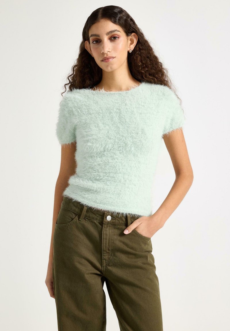 Zelenkavě mátový chlupatý svetr s krátkými rukávy a kulatým výstřihem. Kombinován s olivově zelenými kalhotami s předními kapsami a pasem na knoflíky.