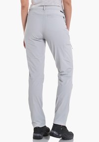 Pantalones de senderismo gris claro hechos de material transpirable. Cuentan con bolsillos laterales con cremallera, un diseño ajustado y un corte recto. Calzado negro visible.