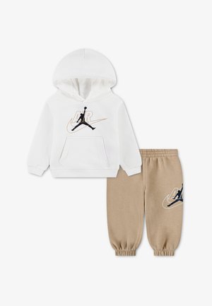 Biała bluza z kapturem z czarnym i złotym logo Air Jordan oraz beżowe spodnie dresowe z elastycznymi mankietami i pasującym logo na lewej nodze.
