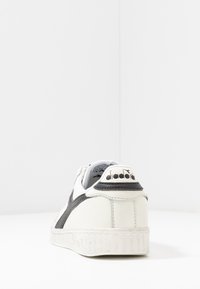 Sneaker bianco con accenti neri, materiale in pelle testurizzata e suola in gomma scanalata. Presenta una linguetta sul tallone con il marchio e una fodera liscia.