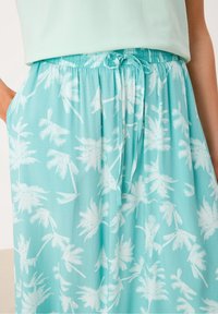 Jupe longue bleu clair avec un motif de palmiers blancs, dotée d'une taille élastique et d'un cordon de serrage pour un ajustement personnalisé.