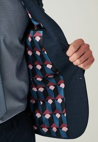 Marineblauwe colbert met een ruitpatroon; interieur heeft een geometrische stof in blauw, roze en zwarte tinten. Lichtgewicht, zachte textuur.