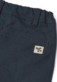 Pantaloni blu scuro con vita elastica, realizzati in tessuto testurizzato e con un'etichetta quadrata color crema con testo nero sulla tasca posteriore.