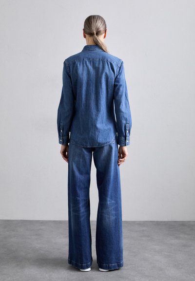 Denim shirt with a pointed collar and buttoned cuffs, paired with wide-leg denim pants. Both are in medium blue, highlighting a consistent texture.