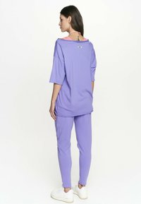 Fioletowy, oversize'owy t-shirt z luźnymi rękawami, w zestawie z pasującymi fioletowymi dresami. Materiał wydaje się być miękki, z luźnym krojem i minimalnym logo.