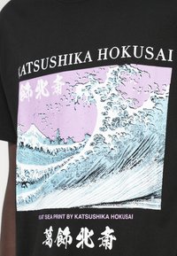 Μαύρο T-shirt με γραφικό κύμα του Χοκουσάι σε ροζ και μπλε χρώματα με ιαπωνικούς χαρακτήρες. Σύντομα μανίκια και κλασικός σχεδιασμός με στρογγυλή λαιμόκοψη.