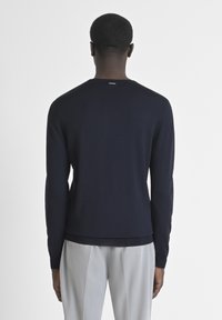 Pullover lungo navy blue in maglia a maniche lunghe con scollo rotondo, polsini e orlo a coste. Presenta un piccolo etichetta del marchio sul retro.