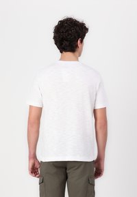 Hvit bomull T-skjorte med korte ermer og rund hals, med et subtilt teksturert mønster, sett fra baksiden. Enkel design.