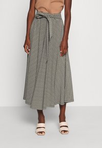 Femme portant une jupe midi à motifs taille haute avec une ceinture nouée, un top sans manches beige et des sandales à talons ouverts beiges.