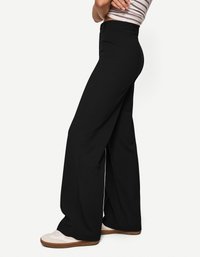 Pantaloni negri cu picioare largi, dintr-un material moale, având talie înaltă și buzunare laterale. Asortați cu adidași de culoare deschisă.