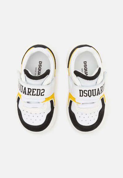 Sneakers bianchi e neri con dettagli gialli, dotati di una fascetta in velcro e dettagli perforati sulla punta. Nome del marchio stampato sulla fascetta.