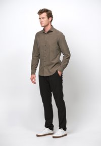 Koszula zapinana na guziki w stonowanym brązie, z długimi rękawami i klasycznym kołnierzykiem, zestawiona z czarnymi spodniami i białymi trampkami. Prosty, elegancki design.