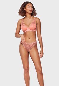 Completo di lingerie in pizzo corallo, con un motivo floreale. Il reggiseno ha un dettaglio a chiave e spalline regolabili; le mutandine hanno un bordo in pizzo a scallop.