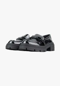 Scarpe in pelle verniciata nera con suola robusta nera, dotate di una fibbia e di un dettaglio a cinturino. Punta rotonda e superficie liscia e lucida.
