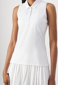 Bílý bezrukávový polo top vyrobený z měkkého materiálu, s klasickým límcem a knoflíkovou légou. Hladká textura s volnějším střihem.