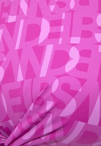 Rosa Stoff mit einem auffälligen Muster aus großen, sich überlappenden Buchstaben in unterschiedlichen Rosatönen, die ein strukturiertes Aussehen erzeugen.