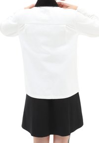 Veste en denim blanc avec un col en velours côtelé noir, manches longues et coupe droite. Le dos présente un design minimaliste sans aucune marque visible.