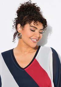 Top con scollatura a V caratterizzato da un ampio design a blocchi di colore in blu navy, rosso e bianco. Tessuto morbido e leggero con maniche trasparenti e rifiniture a contrasto.