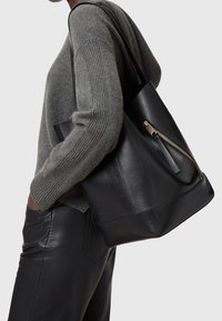 Czarna skórzana torba tote o zwartej konstrukcji, z zamknięciem na zamek w kolorze złotym i akcentem w postaci frędzla. Gładka tekstura z detalem bocznych paneli.