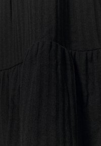 Tissu noir texturé avec des côtes verticales. Comprend une couture froncée pour un détail supplémentaire, mettant en valeur une apparence douce et légèrement volumineuse.