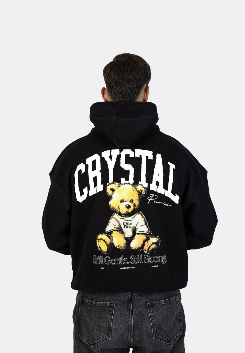 Felpa nera con cappuccio caratterizzata da una grande grafica di un orsetto, il testo "CRYSTAL Paris" e lo slogan "Still Gentle. Still Strong." sul retro.
