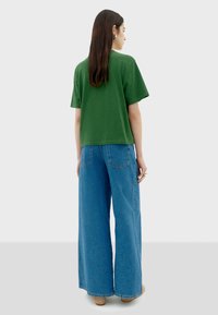 Groene cropped t-shirt in combinatie met wijde blauwe jeans, met een denim textuur en zichtbare achterzakken. Minimalistisch ontwerp met een neutrale achtergrond.