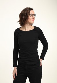 Schwarzes Langarmshirt aus leichtem Stoff mit Rundhalsausschnitt. Kombiniert mit schwarzen Hosen, die eine figurbetonte Passform zeigen.