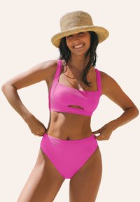 Jasnoróżowy, żeberkowany zestaw bikini z wykrojem z przodu, składający się z krótkiego topu i wysokich majtek, wykonany z gładkiego materiału.