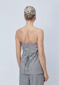 Top grigio senza spalline con scollatura arricciata e dettaglio in vita annodato. Tessuto morbido, vestibilità ampia e un leggero luccichio.
