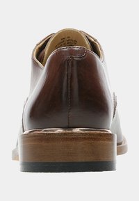 Chaussure habillée en cuir marron avec un bout arrondi, des coutures visibles, et un talon en bois. Texture lisse et design classique avec des accents minimalistes.
